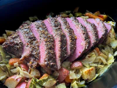 Sliced corned beef brisket on top of cabbage, potatoes, and carrots in a slow cooker.