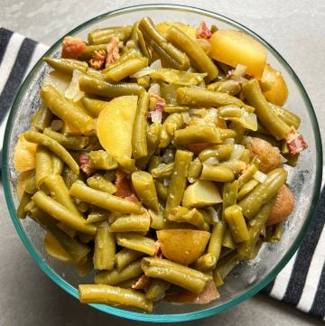 Green beans with bacon and potatoes in glass bowl on top of black and white striped linen.