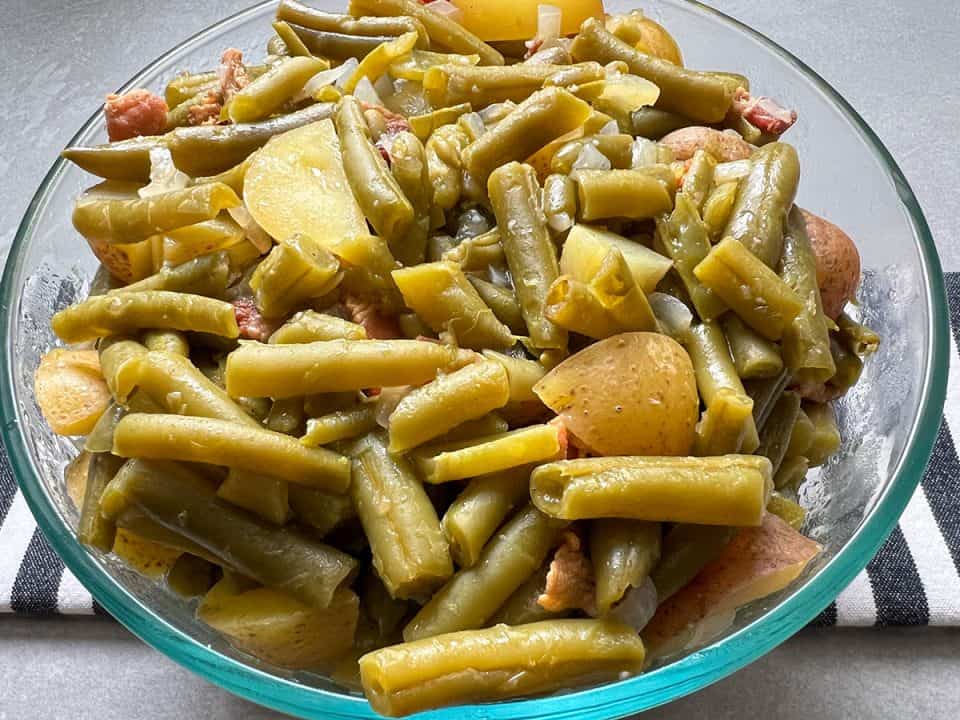 Green beans with bacon and potatoes in glass bowl on top of black and white striped linen.