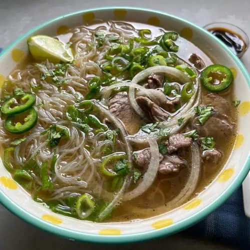 Beef pho in large bowl with polka dots with spoon and chopsticks.