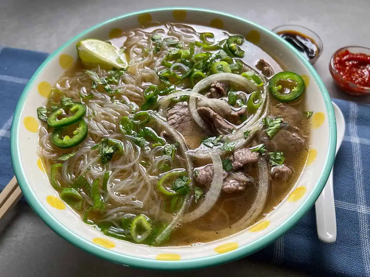 Beef pho in large bowl with polka dots with spoon and chopsticks.