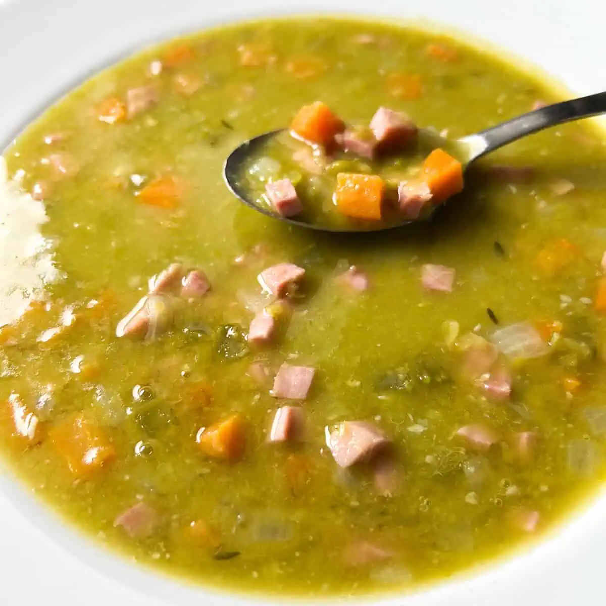 Split pea soup in a white bowl with a spoon on the side