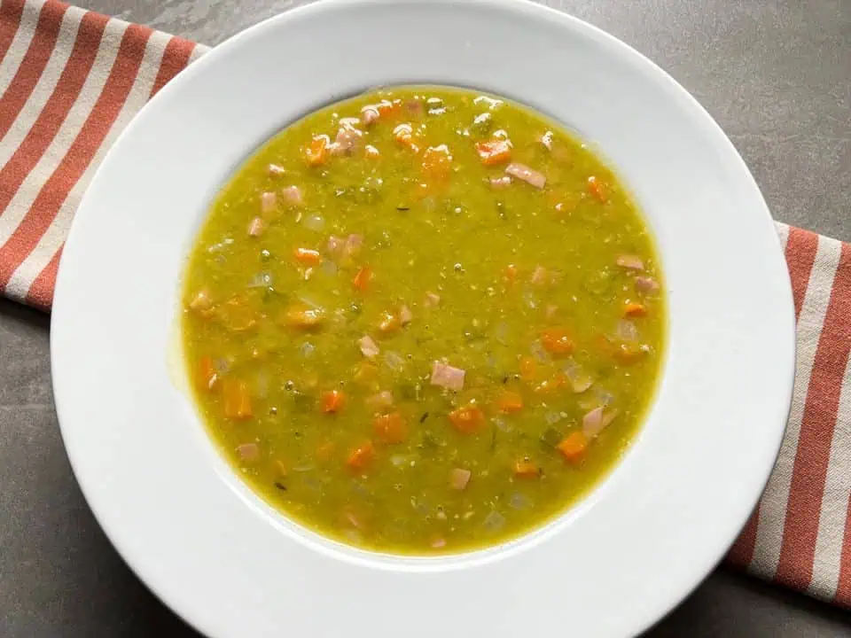 Split pea soup in a white bowl with striped linen in background.