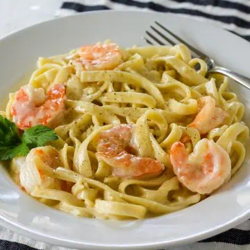 Shrimp alfredo in white rimmed bowl with fork and striped linen.