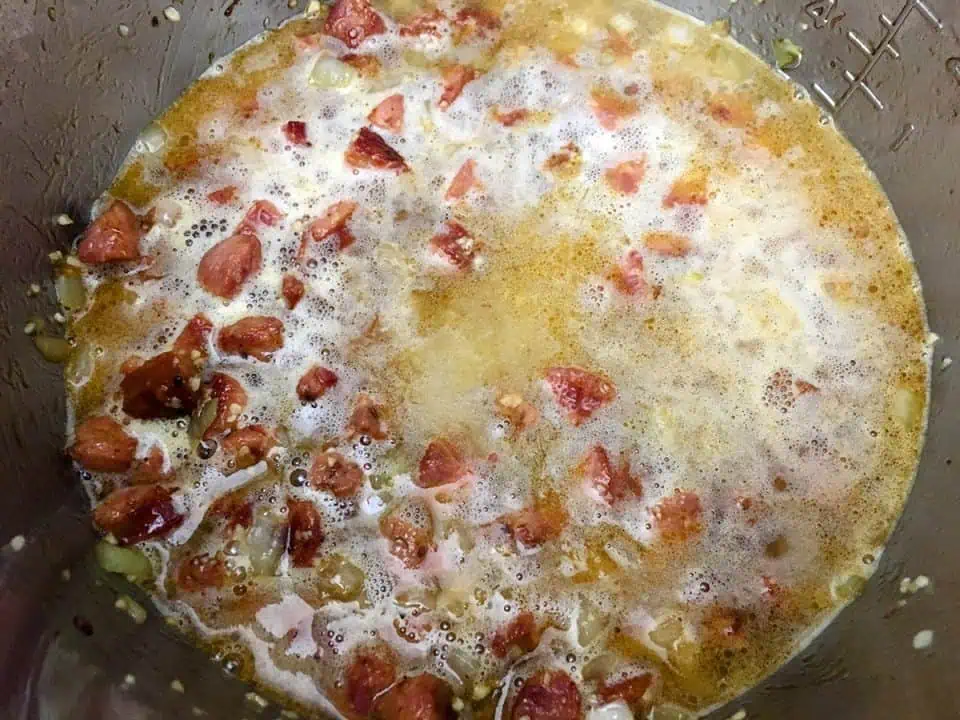 White wine reducing in pot with sausage and onions.
