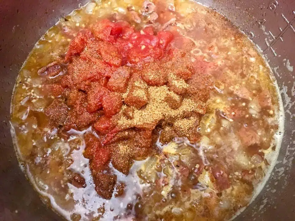 White wine, chopped tomatoes, and Creole seasoning cooking in Instant Pot.