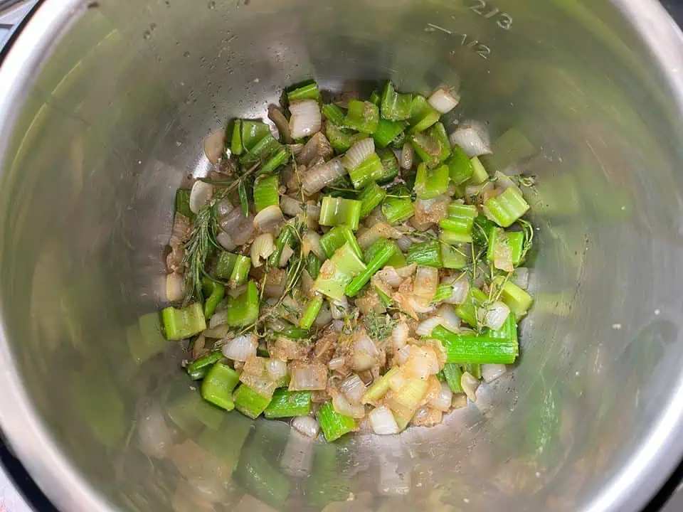 Chopped onions and celery sautéing in Instant Pot with thyme, rosemary, garlic, and a bay leaf.