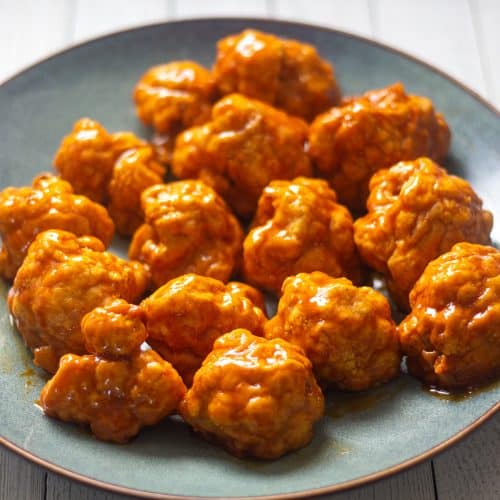 Air fryer cauliflower wings covered in sauce on a gray plate.