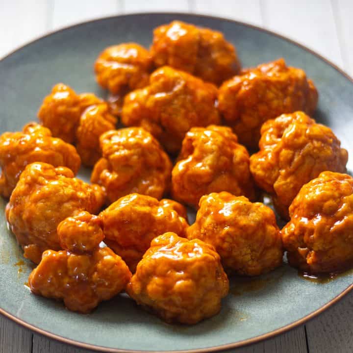 Air fryer cauliflower wings covered in sauce on a gray plate.