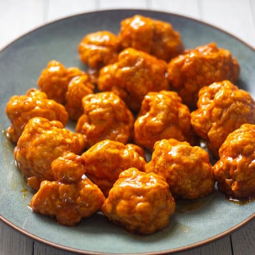 Air fryer cauliflower wings covered in sauce on a gray plate.