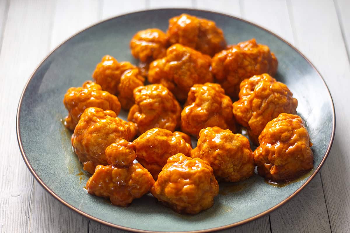 Air fryer cauliflower wings covered in sauce on a gray plate.