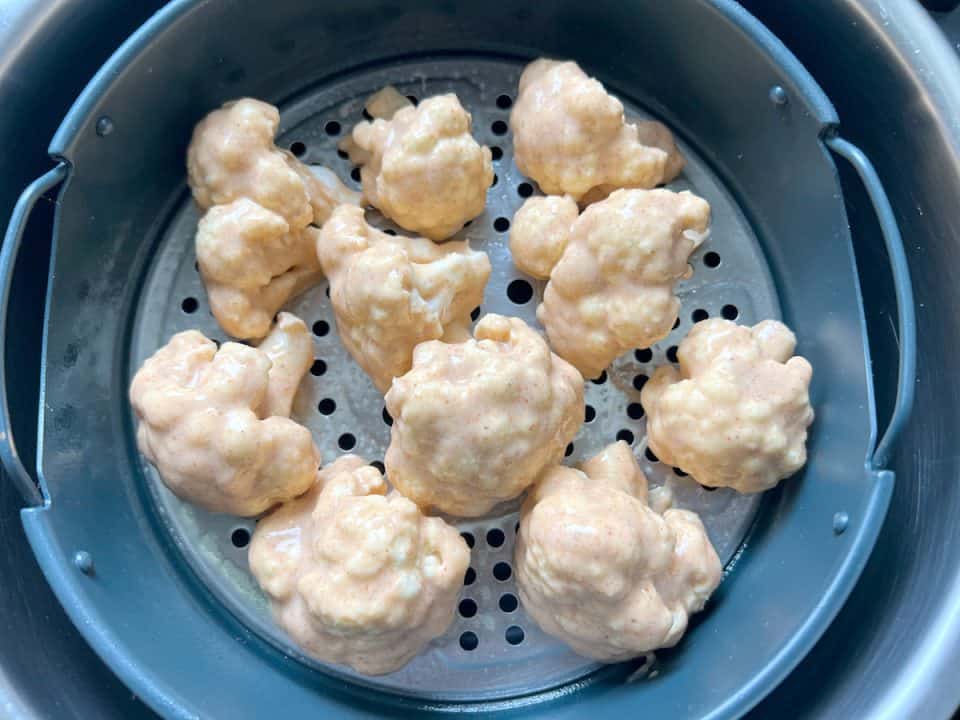 Uncooked, batted cauliflower florets in an air fryer.