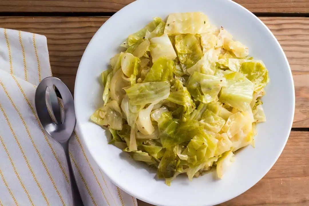 Instant Pot cabbage in white bowl with serving spoon and yellow and white striped linen.