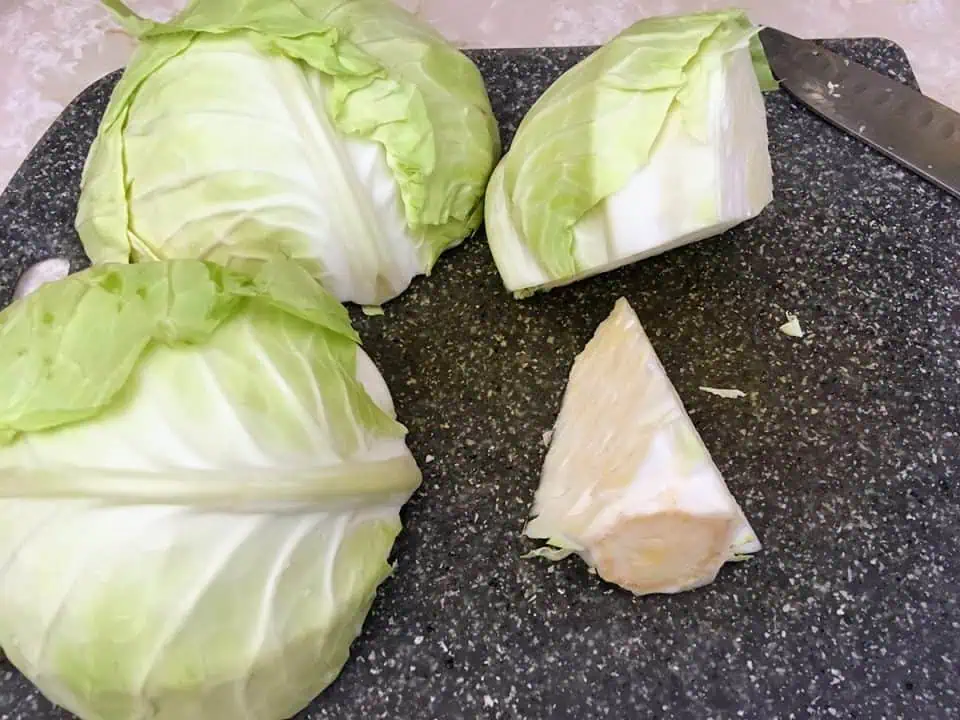 Head of cabbage cut into three pieces with core removed on cutting board.