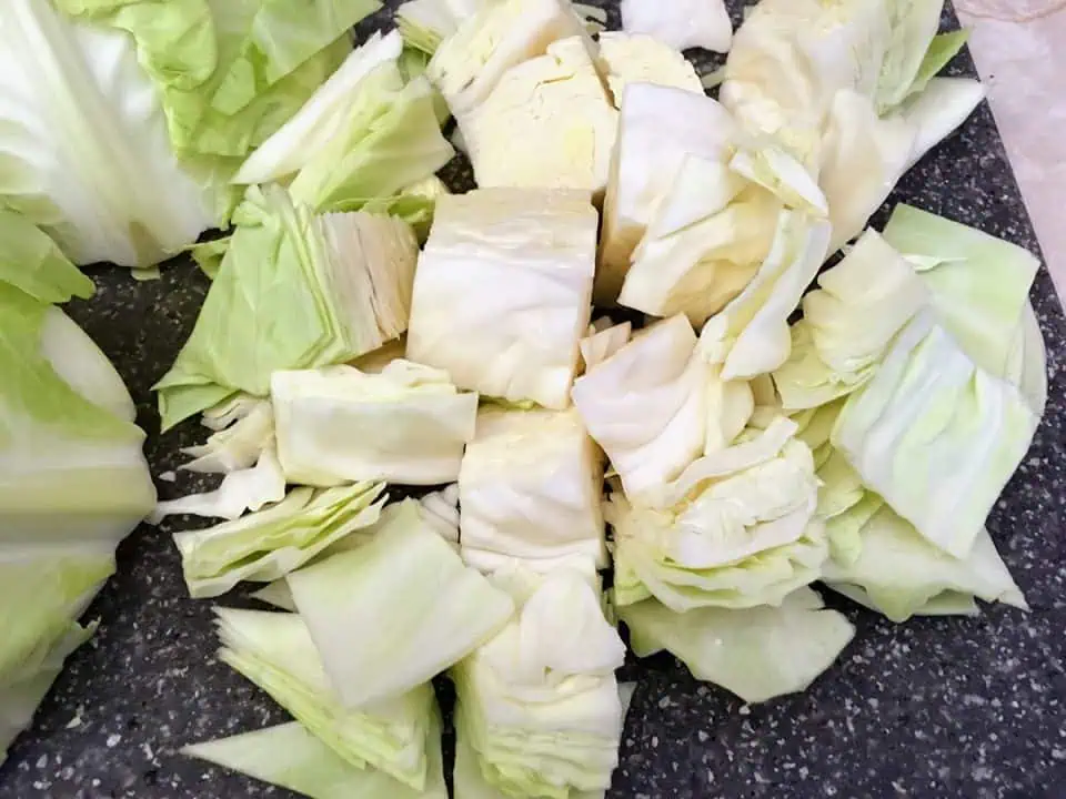 Cabbage on cutting board cut into bite-sized pieces.