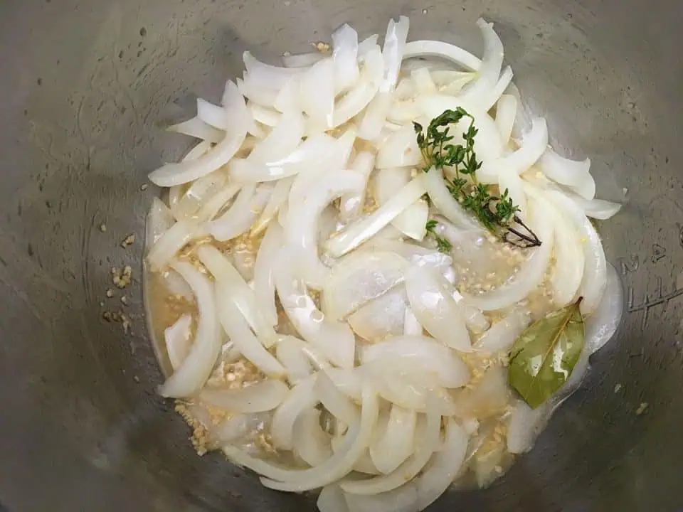 Sauteed onions in Instant Pot with garlic, bay leaf, and thyme spring.