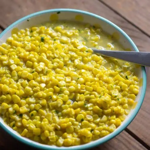 Instant Pot Creamed Corn in white bowl with teal rim and a spoon on wood table.