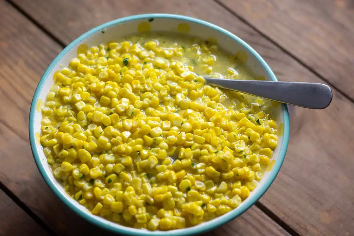 Instant Pot Creamed Corn in white bowl with teal rim and a spoon on wood table.