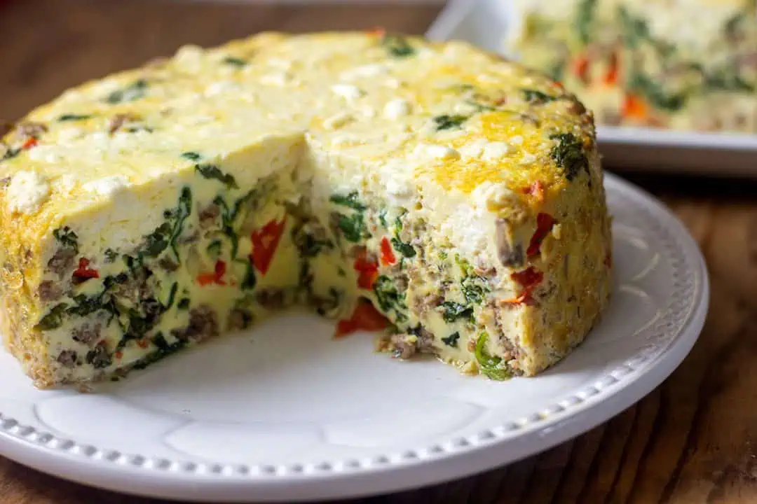 Instant Pot frittata on white plate with large slice cut out on separate plate in the background.