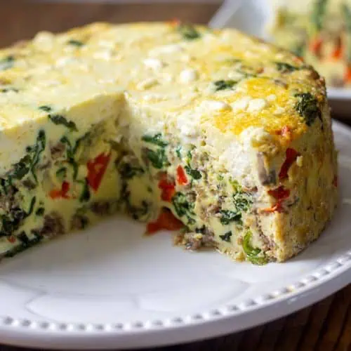 Instant Pot frittata on white plate with large slice cut out on separate plate in the background.