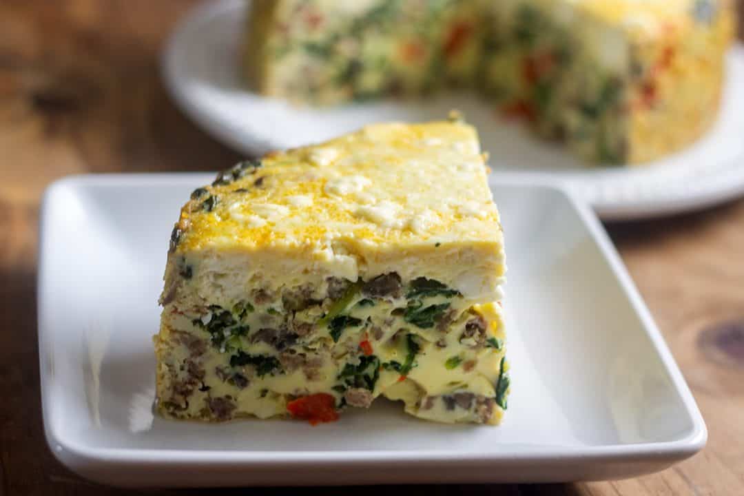 Slice of Instant Pot frittata in small plate with the rest of the frittata in the background.