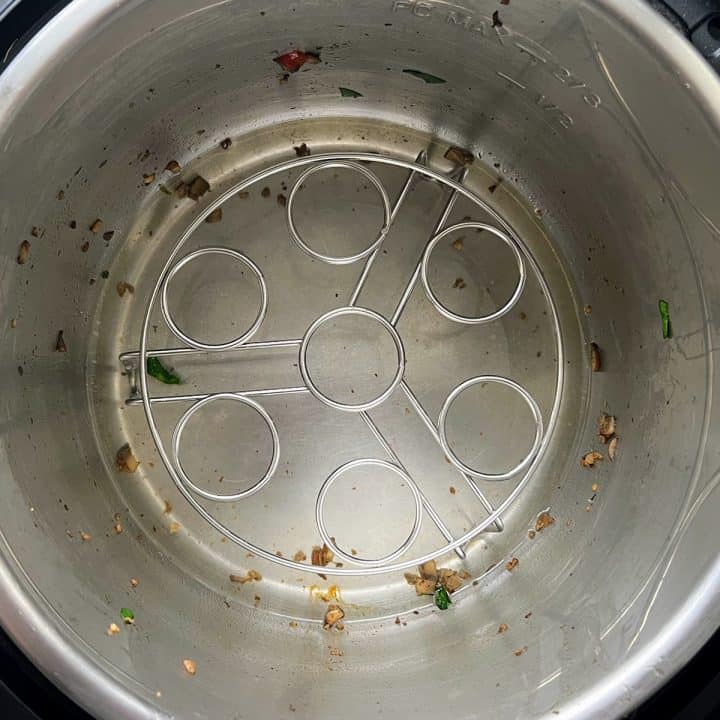 Inside of an Instant Pot with a trivet, a little water, and a few pieces of sautéed veggies.