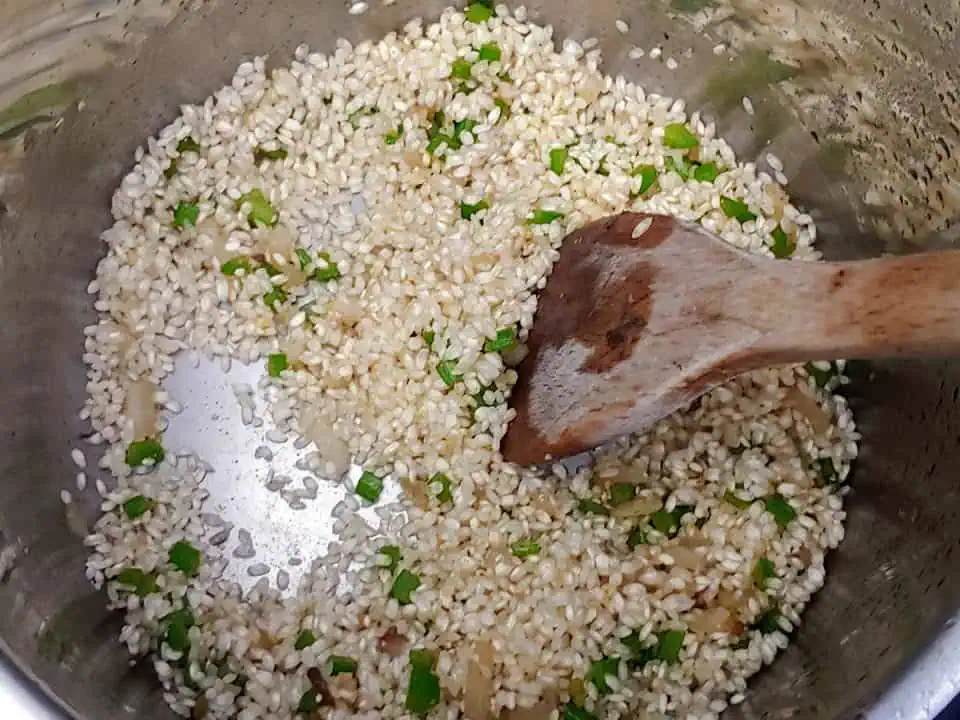Mixing arborio rice with a spatula in pot with onions and celery.