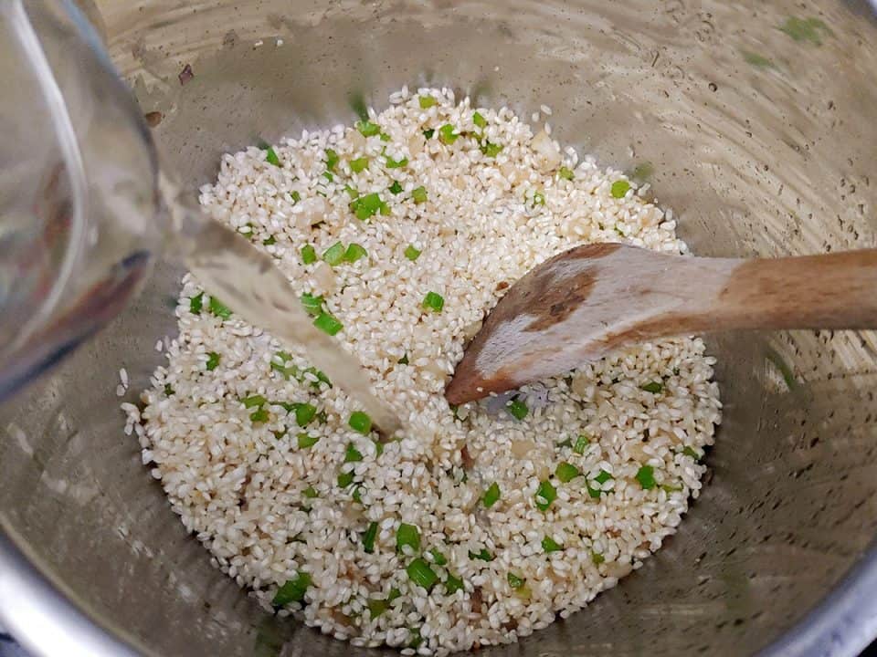 Pouring white wine into pot with uncooked risotto rice.