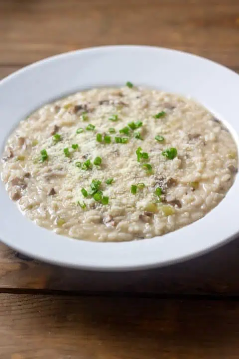 Instant Pot mushroom risotto in white bowl on wood table.