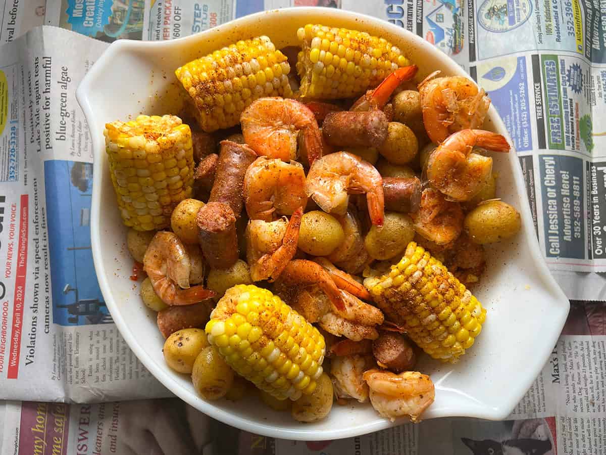 Instant Pot shrimp boil in large white bowl with newspaper background.