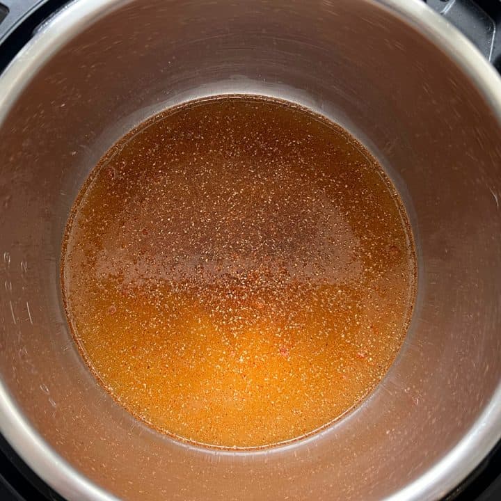 Instant Pot with chicken broth and spice blend in the bottom.