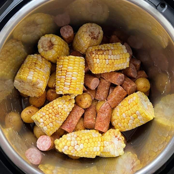 Uncooked corn, sausage, and potatoes topped with spice blend in Instant Pot.