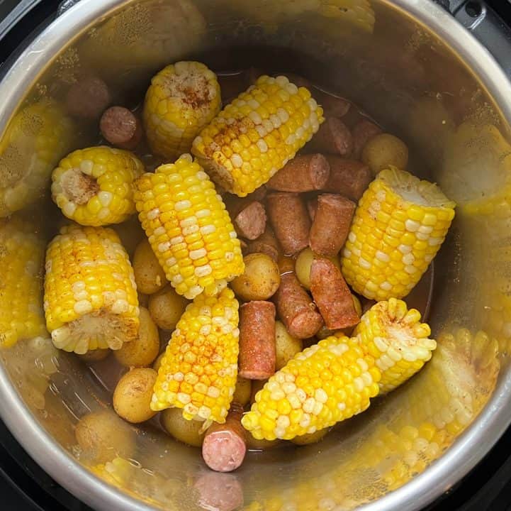Cooked corn, sausage, and potatoes topped with spice blend in Instant Pot.