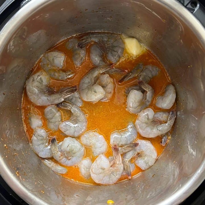 Uncooked shrimp and butter in broth in bottom of pot.