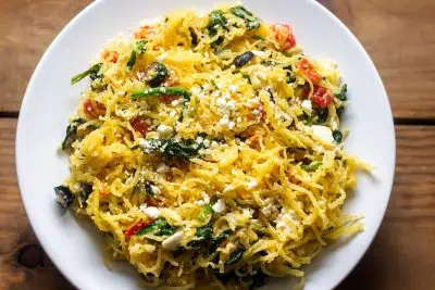 Greek-style spaghetti squash in white rimmed bowl on wood table.