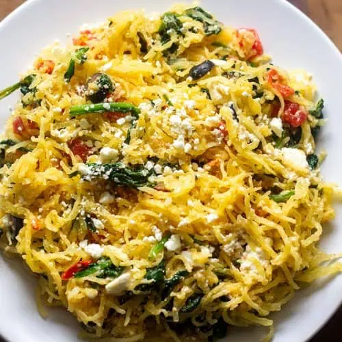 Greek-style spaghetti squash in white rimmed bowl on wood table.