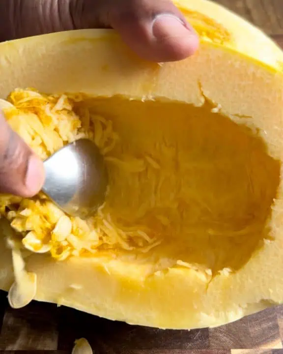 Scooping out seeds from a spaghetti squash with a spoon.