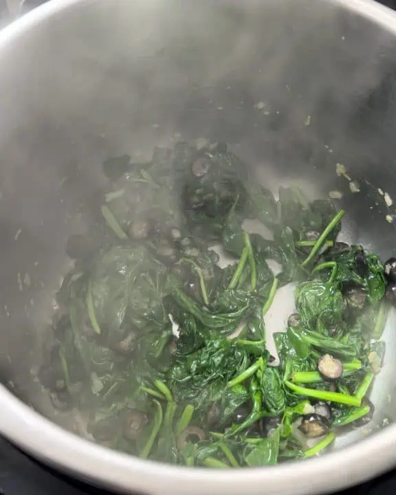 Spinach wilting in Instant Pot with onions and olives.