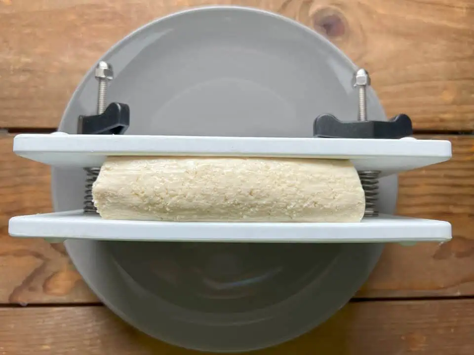 Pressing tofu in a tofu press on a gray plate on wood table.