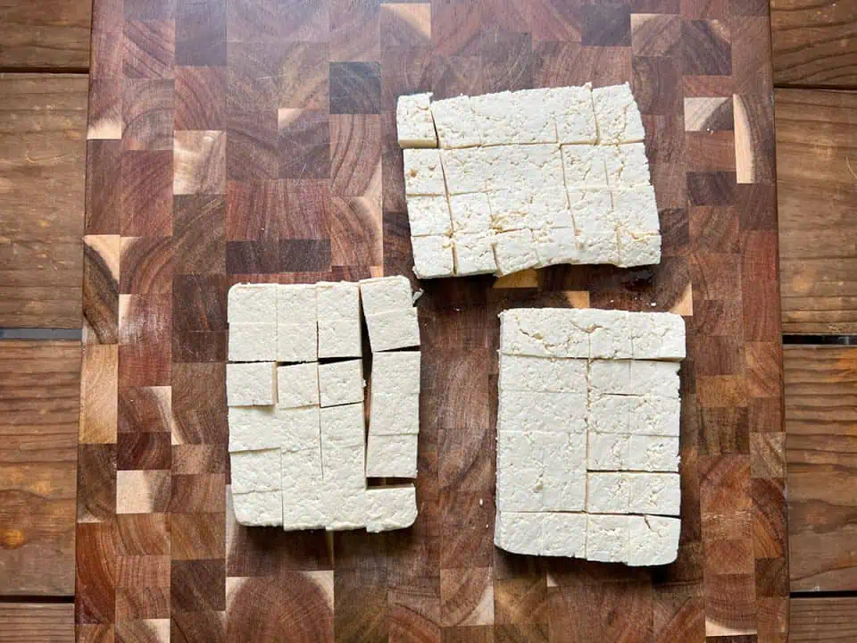 Tofu cut into small cubes on a wooden cutting board.