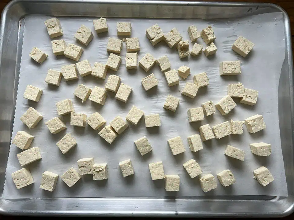 Small cubes of uncooked tofu on a baking sheet lined with parchment paper.