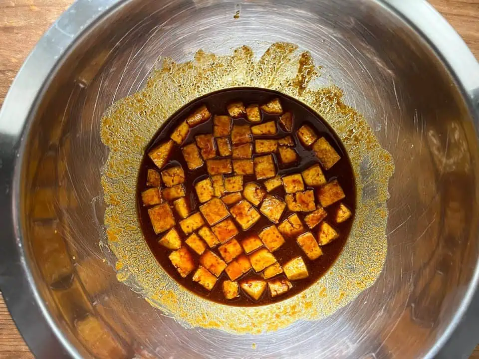 Small cubes of tofu marinating in sauce in a large mixing bowl,