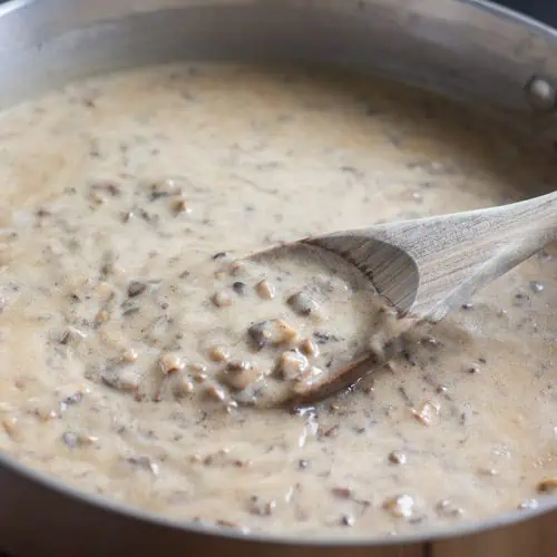 Vegan cream of mushroom soup in a large pan with a mixing spoon on wood table.