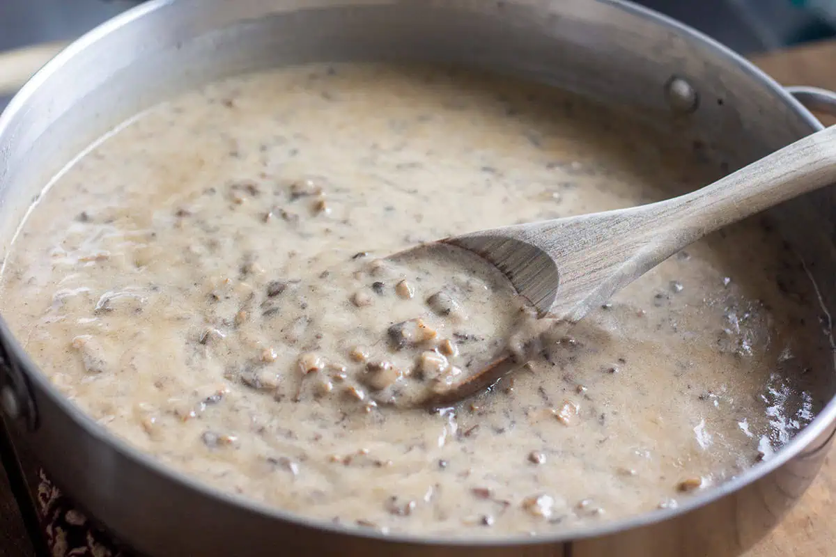 Vegan cream of mushroom soup in a large pan with a mixing spoon on wood table.