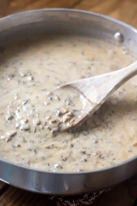 Vegan cream of mushroom soup in a large pan with a mixing spoon on wood table.