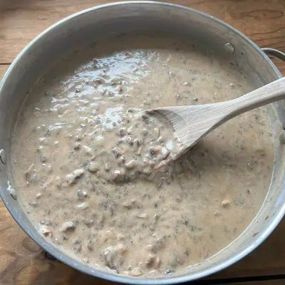 Vegan cream of mushroom soup in a large pan with a mixing spoon on wood table.
