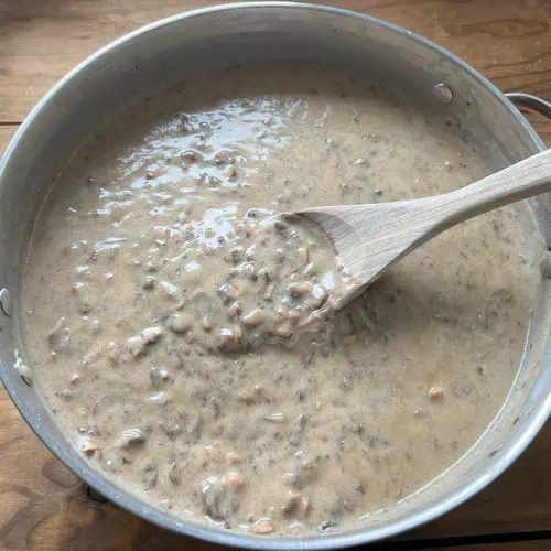 Vegan cream of mushroom soup in a large pan with a mixing spoon on wood table.
