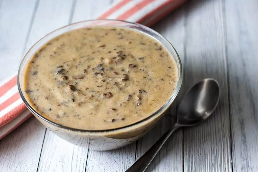 Bowl of vegan cream of mushroom soup on white wood table with striped linen.