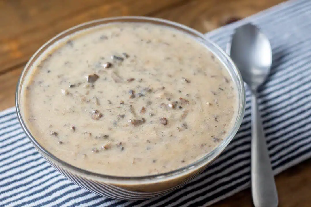 Bowl of vegan cream of mushroom soup on wood table with striped linen.