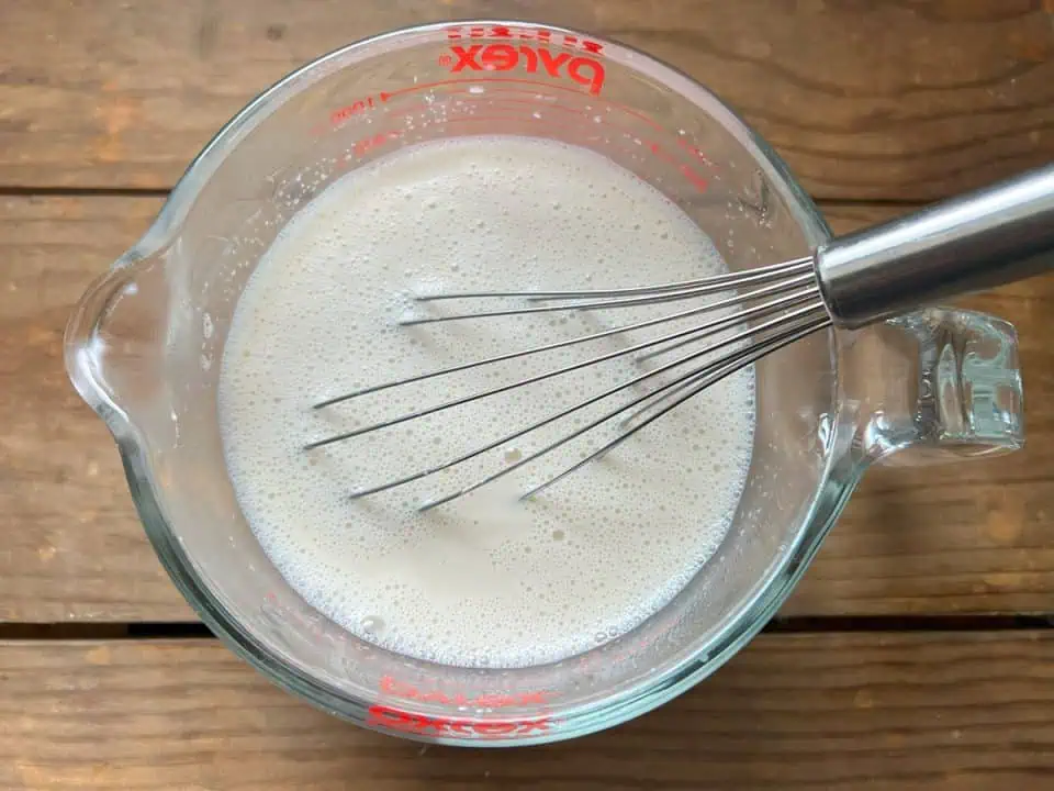 Cornstarch and milk slurry in a measuring cup with a whisk.